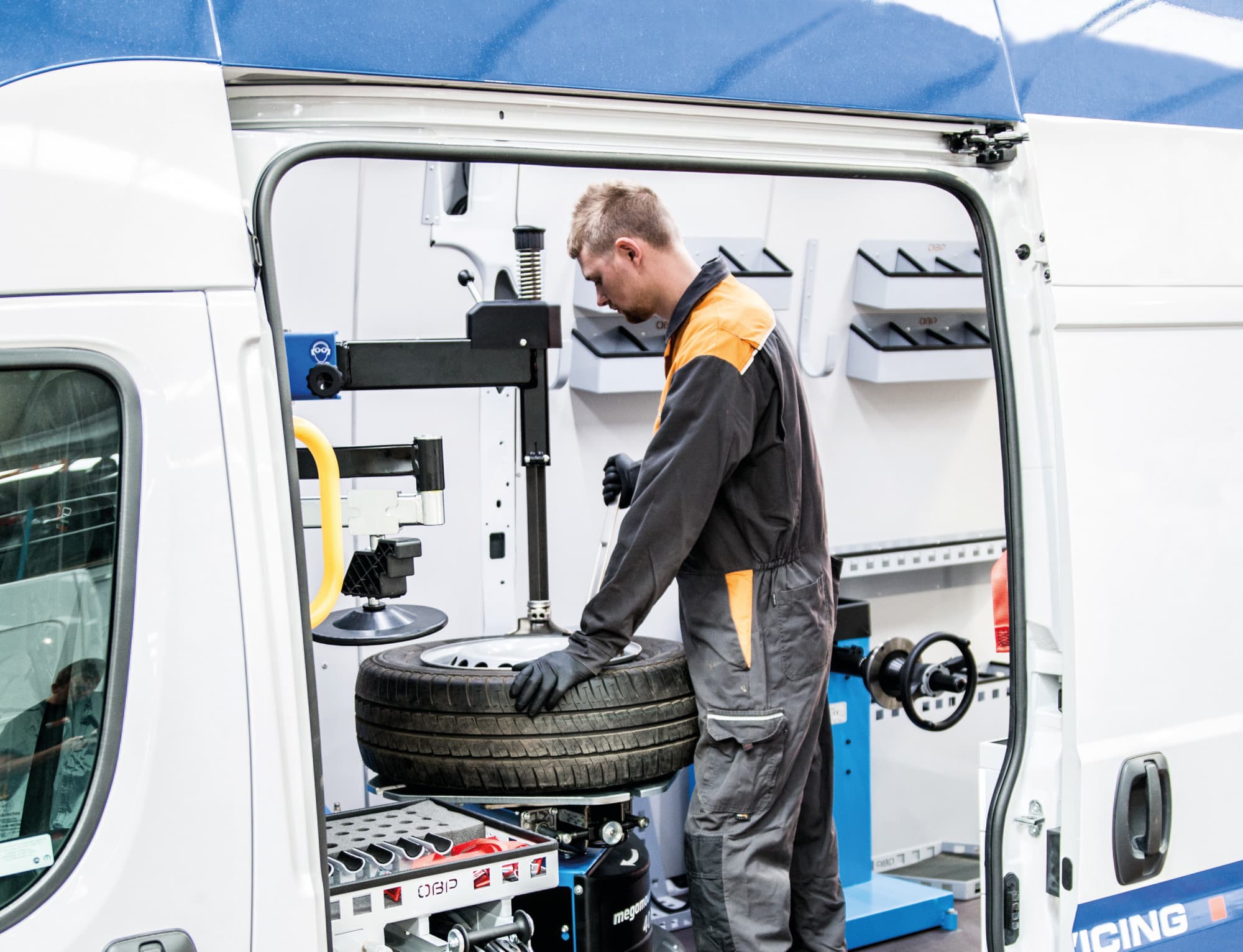 A technician in overalls working a tyre on the tyre-changing machine built into the back of a van